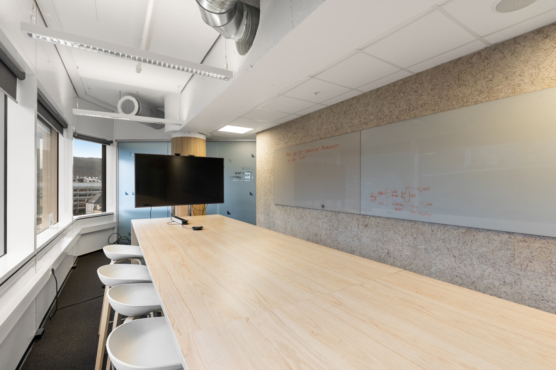 A large HUB workshop room with a long wooden table, whiteboard wall and a display.