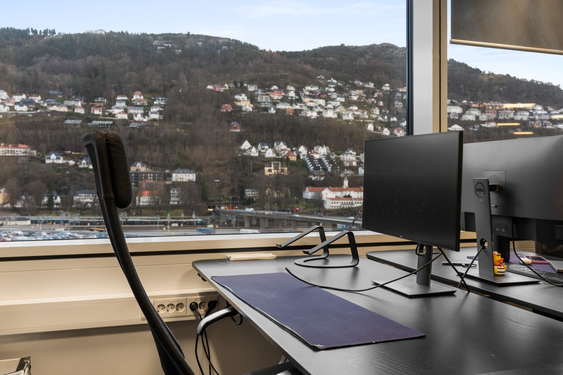 A HUB office desk with dual monitors and a panoramic view of Bergen's hillsides.